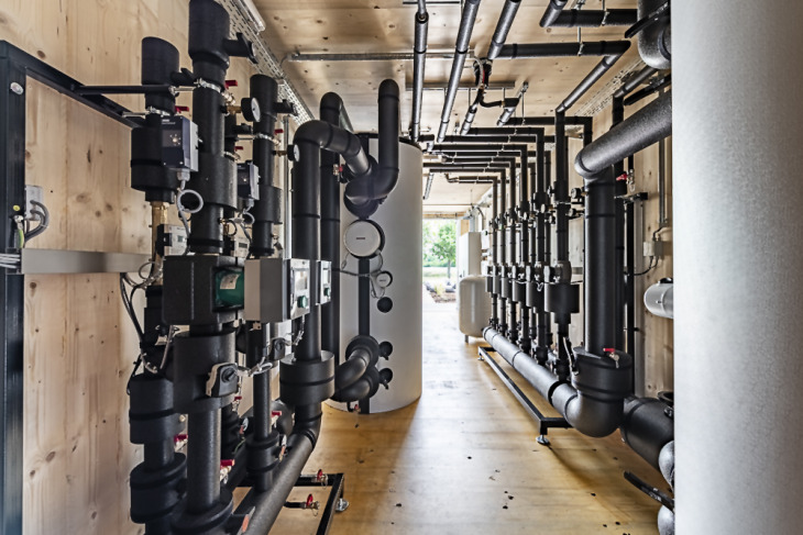 Innenansicht einer Energiezentrale im Holzcontainer mit Übergabestationen, Speicher und Rohrverbindungen