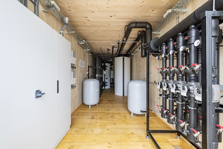 Innenansicht einer Energiezentrale im Holzcontainer mit Schaltschrank, Pufferspeichern und Heizungsverteiler